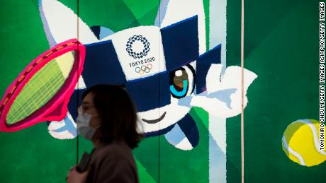Un peatón con una máscara facial pasa la exposición con una ilustración de la mascota de los Juegos Olímpicos y Paralímpicos Miraitov 2020 26 de febrero de 2020. En Tokio, Japón. 