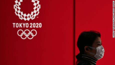 Una mujer con una máscara facial pasa por la pantalla con el logotipo de los Juegos Olímpicos de Tokio 2020 en Tokio el 24 de marzo de 2020.