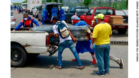 Hombres con trajes protectores cargan un ataúd en un automóvil frente al hospital de Guayaquil.