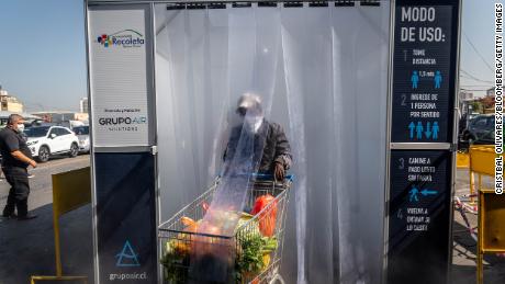 Una persona con una máscara protectora empuja un carrito de compras a través de una cámara de desinfección en el mercado central de frutas y verduras de La Vega en Santiago, Chile.