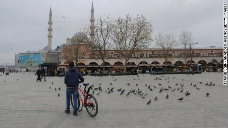 Un hombre con una bicicleta rodeado de palomas en la plaza Yenicami casi vacía, en el Bazar de las Especias en Estambul, Turquía, durante un bloqueo de fin de semana.