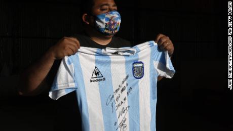 El hombre sostiene una réplica de la camiseta del equipo de fútbol argentino utilizada durante la final de la Copa del Mundo de 1986 y firmada por Diego Maradon.