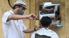 Un peluquero en la carretera que se pone una máscara facial le corta el pelo a un cliente en Hanoi.