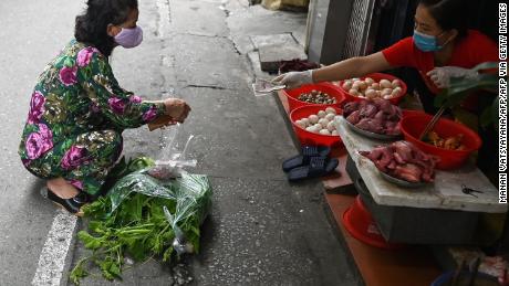Una mujer practica la distancia social mientras compra detrás de la línea en un mercado húmedo en Hanoi.