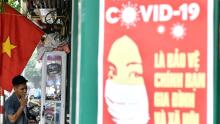 Un cartel de propaganda sobre la prevención de la propagación del coronavirus es visible en la pared cuando un hombre fuma un cigarrillo en una calle de Hanoi.