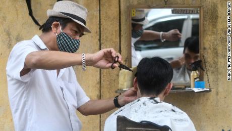 Un peluquero en la carretera que se pone una máscara facial le corta el pelo a un cliente en Hanoi.