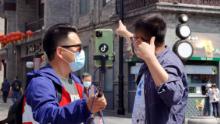 Las personas con máscaras transmiten en vivo en la calle Qianmen el 25 de abril en Beijing, China.
