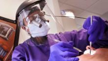 Dentista Kathleen Saturay usa equipo de protección adicional, incluyendo un protector facial y una máscara de respirador desechable, mientras trabaja con un paciente en Seattle.
