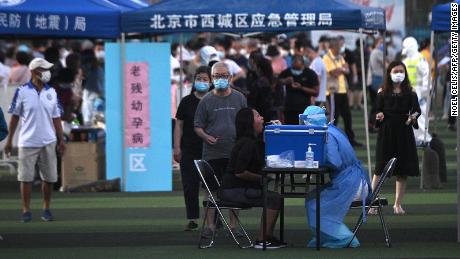Un trabajador de la salud con un mono protector realiza una prueba de frotis de una mujer en un centro de pruebas establecido para personas que visitaron o viven cerca del mercado Xinfadi en Beijing.